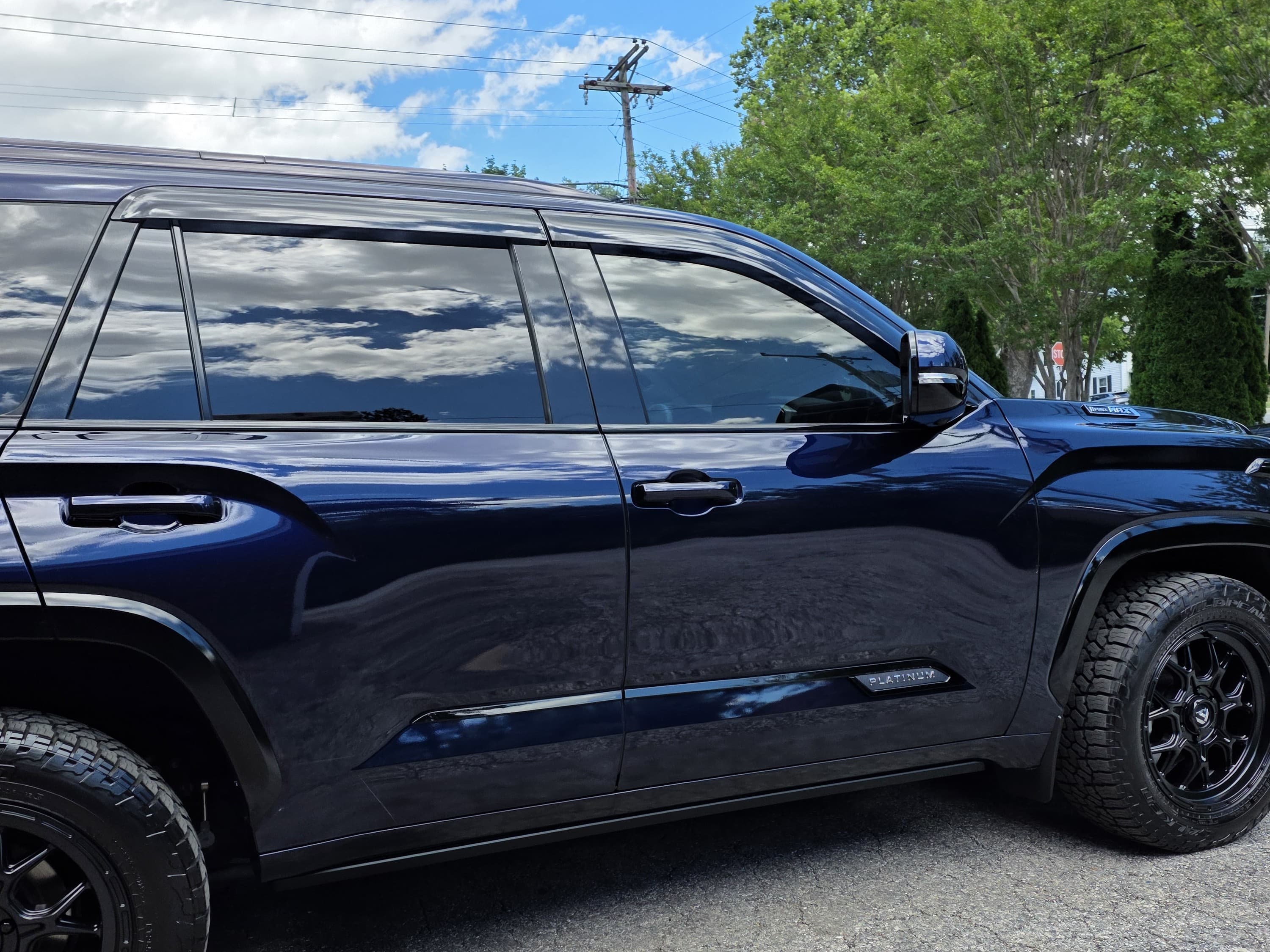 The full glossy side profile of a navy Toyota Sequoia after a ceramic coating, sky and clouds mirrored in the paint, in Carroll County, MD